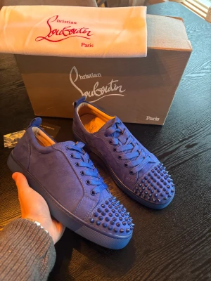 Christian Louboutin sneakers med allt og - Snygga blå sneakers från Christian Louboutin i mocka med matchande blå snörning och coola nitar på tån. Insidan är beige och yttersulan har den klassiska röda Louboutin-loggan. Kommer med extra nitar och originalkartong.