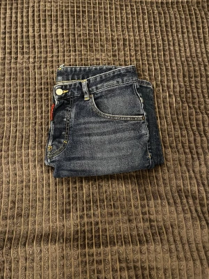 Dsquared2 jeans  - Snygga mörkblå jeans från Dsquared2 med skinny passform och klassisk femficksdesign. Jeansen har gul kontrastsöm, Dsquared2-logga på röd etikett vid gylfen och läderpatch bak i midjan. Materialet är slitstarkt denim med lätt tvättad look.