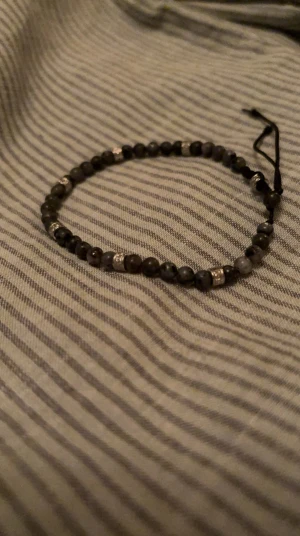 Svart pärlarmband med silverdetaljer - Stilrent armband med små svarta pärlor och diskreta silverfärgade detaljer. Armbandet har en justerbar snörning som gör det enkelt att anpassa storleken. Perfekt för dig som gillar minimalistiska accessoarer med en touch av metall.