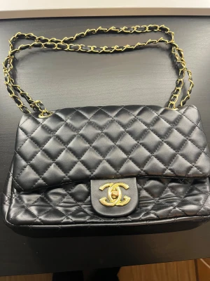Svart quiltad cc axelväska - Säljer en ikonisk svart axelväska  med klassiskt quiltat mönster och guldfärgad kedja. Väskan har den välkända CC-loggan i guld på framsidan och är tillverkad i mjukt skinn. Perfekt storlek för det viktigaste och en riktig statement piece.