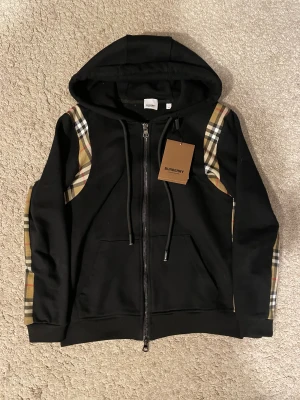 Svart Burberry hoodie  - Säljer denna riktiga trendiga burberry hoodien. Den är storlek M och bara använd ett fåtal gånger och det finns inga konstigheter med den alls.