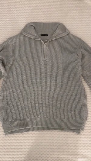 Grå stickad half zip tröja från SHEIN - Snygg grå stickad tröja från SHEIN i storlek M. Tröjan har en ribbad struktur, hög krage och en cool half zip-dragkedja med ringdetalj. Långärmad och loose fit, perfekt för chill höst- och vinterdagar. Passar dig som gillar enkel och stilren vibe.