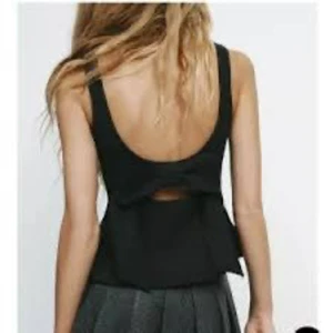 Svart linnetopp med rosett i ryggen - Snygg svart linnetopp med breda axelband och öppen rygg. Toppen har en stor rosett baktill och en liten öppning under rosetten som ger en cool detalj. Passformen är normal och materialet känns som polyester. Perfekt för dig som gillar stilrena och trendiga plagg🥰🥰