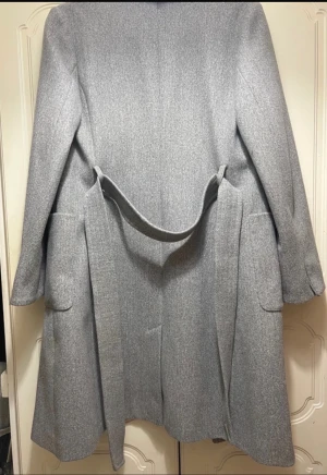 Grå kappa Dorothy Perkins med bälte - Stilren grå kappa från Dorothy Perkins med klassisk krage, knappar framtill och bälte i midjan. Kappan har stora fickor och är helfodrad för extra komfort. Perfekt för dig som vill ha en tidlös look med snygg passform. (Inga defekter eller liknande)