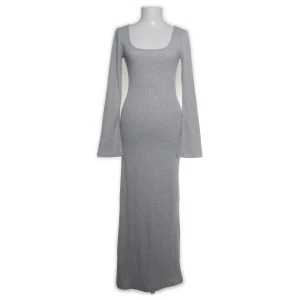 Grå ribbad långklänning från Nelly - Snygg grå långklänning från Nelly med ribbad struktur och långärmade, lätt utsvängda ärmar. Klänningen har en rundad, djup urringning och är figurnära med stretchigt material i polyester, viskos och elastan. Perfekt för dig som gillar stilrena och bekväma plagg.