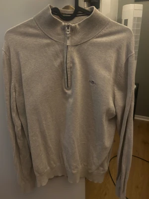 Beige half zip tröja från GANT - Snygg beige långärmad tröja från GANT med ribbad hög krage och half zip-dragkedja framtill. Diskret GANT-logga broderad på bröstet. Mjuk bomullskvalitet och klassisk passform som funkar till många stilar. Köpt för 699kr