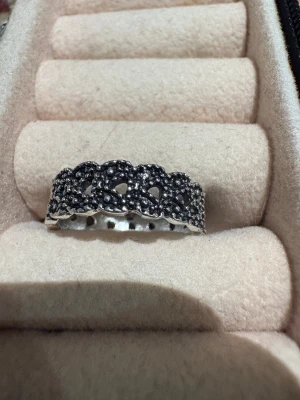 Silverfärgad ring med pärldetaljer - Unik silverfärgad ring med pärldetaljer och ett mönster av små hjärtan runt hela bandet. Ringen har en bred form och en cool, lite vintage vibe tack vare de mörka inslagen mellan pärlorna. Perfekt för dig som gillar statement-smycken med extra edge.