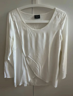 Vit omlottblus från VILA - Säljer en stilren vit omlottblus från VILA med lång ärm och rund halsringning. Blusen har en snygg omlottdetalj framtill som ger en cool och flowy look. Materialet är mjukt och har ett lätt fall, perfekt för att lyfta din outfit