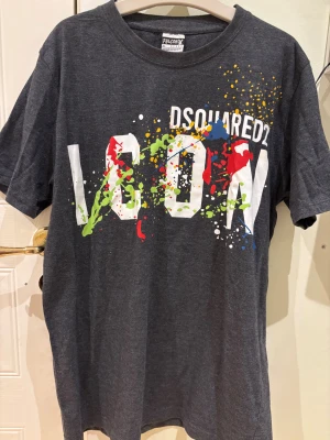 Mörkgrå Dsquared2 ICON t-shirt - Snygg mörkgrå t-shirt från Dsquared2 med stor vit 'ICON'-text och färgstänk i rött, grönt, gult och blått framtill. Klassisk rund hals och korta ärmar. Perfekt statement-plagg för dig som gillar streetstyle.