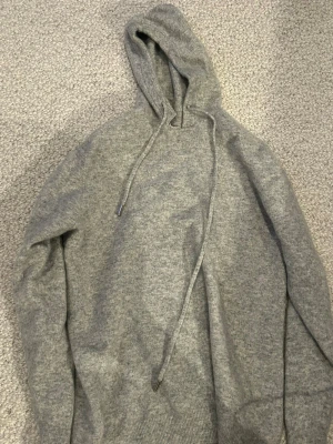 Grå Kashmir hoodie från rexstilo - Mysig grå hoodie med huva och snörning från rexstilo, tillverkad inte längre och har hög efterfrågan. Tröjan är i storlek M men har krympt i tvätten och passar mer som XS. Kragen har också skadats lite men märks inte så mycket!