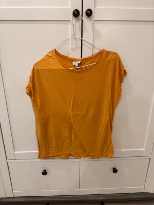 Gul topp från AWARE by Vero Moda - Snygg gul topp från AWARE by Vero Moda i storlek M. Modellen är enkel med rund halsringning och korta ärmar. Tillverkad i mjuk bomull som känns skön mot huden. Perfekt för dig som gillar färg och vill ha en basic topp med lite edge.