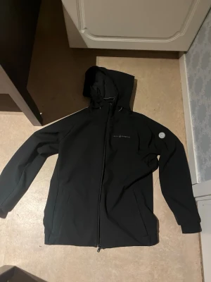 Svart vindjacka från Sail Racing (Båda för 400) - Svart vindjacka från Sail Racing med huva och hel dragkedja framtill. Jackan har diskreta logodetaljer på ärm och huva samt två sidofickor. Insidan har en kontrast i gult. Perfekt för dig som gillar stilren och funktionell design.  Säljer båda för 400