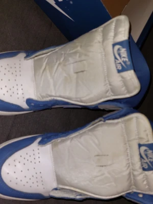 Nike Air Jordan 1 blå/vit strl 43 - Nike Air Jordan 1 sneakers i blått och vitt med klassisk snörning och rund tå. Skorna har en platt sula och är tillverkade i skinn med blå detaljer och vit bas. Snygg retrostil med Nike Air-logga på plösen. Perfekt för dig som gillar streetwear och ikoniska sneakers. Kartong ser inte allra bäst ut men skorna är huvudsaken. Snören saknas men går att fixa för en tjuga på nån affär