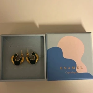 Guldiga örhängen från Enamel Copenhagen - Säljer ett par unika örhängen från Enamel Copenhagen i guld med gröna detaljer. De har en cool, organisk form och är perfekta för att lyfta vilken outfit som helst. Kommer i originalask och aldrig använda.