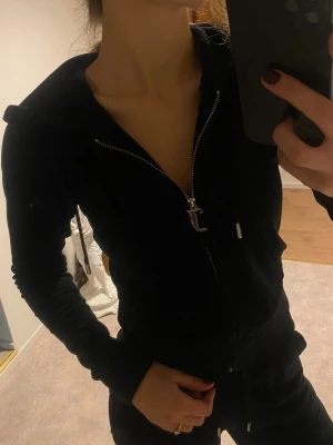 Juicy Couture Kofta svart - Svart hoodie från Juicy Couture i mjuk velour med dragkedja och huva. Snygga snören med metalldetaljer och klassisk JC-logga på bröstet. Mycket fint skick! Går att köpa byxan till också! Skriv>>