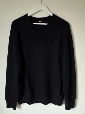 Mörkblå stickad tröja från Uniqlo - En stilren mörkblå stickad tröja från Uniqlo i storlek M. Tröjan har rund hals och långa ärmar, perfekt för lager på lager under kyliga dagar. Materialet är mjukt och bekvämt, vilket gör den enkel att matcha med jeans eller chinos. 5N11
