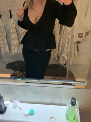 Svart omlottblus med snörning från Nelly - Säljer en svart omlottblus från Nelly i storlek XS. Blusen har långa ärmar, v-ringad hals och snygg snörning i midjan. Den har volang nedtill och är tillverkad i ett lätt, ribbat syntetmaterial. Perfekt för dig som gillar trendiga och feminina detaljer.