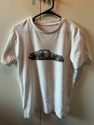 Donce de la sense T-shirt (säljs inte längre) - Vit t-shirt i bomull i storlek xs passar även S, med ett svart tryck av en sportbil och texten 'D'once De La Sense' på bröstet. Klassisk rund halsringning och korta ärmar. Perfekt för dig som gillar bilar och vill ha en enkel men cool look. T-shirten är i bra skick och har inga defekter 
