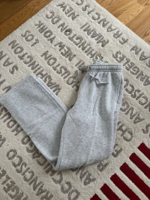 Grå mjukisbyxor från Gina Tricot - Säljer ett par ljusgrå mjukisbyxor från Gina Tricot i storlek S. Byxorna har normal passform, raka ben och resår med snörning i midjan. Tillverkade i mjukt bomullsmaterial som är skönt mot huden. Perfekta för chill dagar hemma eller när du vill vara extra comfy.