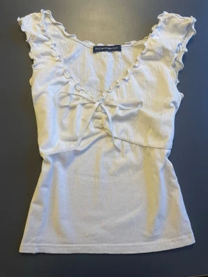 Brandy Melville top - Söt vit topp köpt från Brandy Melville i onesize (skulle säga S-M) 💞 Toppen sitter smickrande på kroppen och på framsidan finns ett vitt sidenband som knyts till en rosett 🤍 Den har en pytteliten grå fläck på framsidan men den syns knappt! 