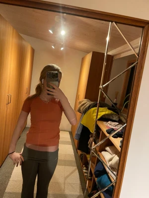 Kortärmad orange topp i bomull - En enkel och snygg kortärmad topp i en varm orange färg. Modellen är figurnära med rund halsringning och ribbade kanter. Perfekt att matcha med jeans eller kjol för en chill look.