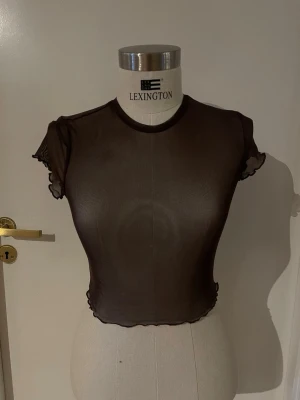 Svart mesh croppad topp - Säljer en svart, transparent mesh topp med korta ärmar och volangkant vid ärmslut och nederkant. Toppen är croppad och har en rund halsringning. Perfekt för att styla lager på lager eller med ett snyggt linne under.