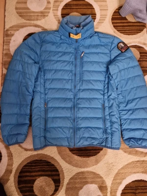 Blå dunjacka från Parajumpers - Säljer en blå dunjacka från Parajumpers i storlek M. Jackan har quiltad design, hög krage och flera dragkedjeförsedda fickor. Märkets patch sitter på ärmen och jackan är superlätt, perfekt för kyliga dagar. Grym stil och funktion i ett!