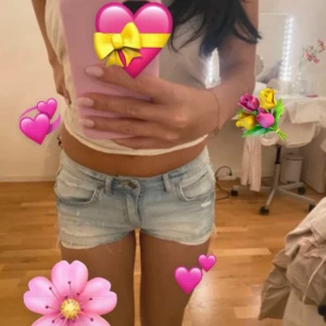 Ljusblå denimshorts - Säljer ett par ljusblå denimshorts med låg midja. Shortsen har klassiska fem fickor och en liten sliten detalj framtill. Perfekta för varma dagar och chill häng.