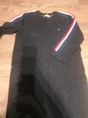 Svart klänning Tommy Hilfiger XS - Svart långärmad klänning från Tommy Hilfiger i storlek XS. Snygga ränder i rött, vitt och marinblått längs axlarna och ärmarna. Rund halsringning och mjukt stickat material som känns skönt mot huden. Liten logga på bröstet för extra stil. Den har en liten fläck på framsidan, men inget man märker. Se sista bild! Den är endast använd ett fåtal gånger. 😊