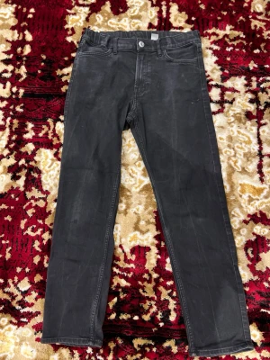 Svarta slim fit jeans från H&M - Svarta jeans från H&M i slim fit-modell med justerbar midja. Klassisk femficksdesign och knappstängning framtill. Snyggt smal passform som sitter tajt längs benen och passar perfekt till en modern stil.