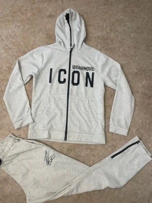 Grå mjukisbyxor DSQUARED2 ICON - Snygga grå mjukisbyxor från DSQUARED2 ICON med svart dragkedja vid fickan och elastisk midja. Byxorna har en cool autografdetalj och är gjorda i mjukt bomullsmaterial som är perfekt för chill dagar. Passar dig som gillar streetwear och vill sticka ut.