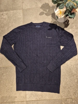 Mörkblå stickad tröja från Bondelid - Säljer en mörkblå kabelstickad tröja från Bondelid, modell Dave cable crew neck. Tröjan har rund hals, långärmade ribbade muddar och ett diskret broderat Bondelid-logo på bröstet. Perfekt för dig som gillar klassisk och stilren design.