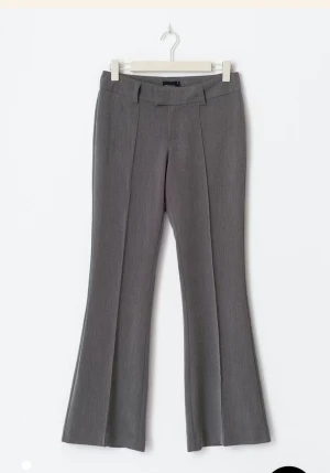 Grå  bootcut tall  kostymbyxor -  Jag köpte dessa i tall de sitter jätte bra och långa jag är 166. Snygga grå kostymbyxor med bootcut-snitt och pressveck framtill. Byxorna har bälteshällor och klassisk midja, perfekta för en stilren look. Materialet är mjukt och har en lätt struktur som ger en dressad känsla.