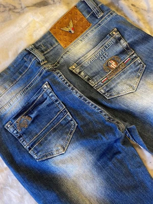 Blå jeans från Philipp Plein - Snygga blå jeans från Philipp Plein med coola broderade detaljer på bakfickorna och logotyp på läderpatchen. Jeansen har en klassisk femficksdesign, slitningar och ljusa tvättade partier som ger en fräsch vibe. Passar dig som gillar street och exklusiv stil.