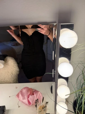 Svart kort klänning med snörning - Supersnygg svart kort klänning med smala axelband och v-ringning. Klänningen har snörning framtill och rynkade detaljer längs hela framsidan som ger en riktigt schysst passform. Perfekt för dig som gillar en tight och stilren look.