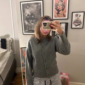 Grå stickad kofta med knappar  - Mysig grå stickad kofta med rund hals och stora knappar framtill. Koftan har lång ärm och ribbade muddar vid ärmslut och nederkant. Perfekt att slänga på sig när det är kyligt ute.