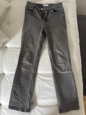 Grå raka jeans från Zara, strl 36 - Säljer ett par grå jeans från Zara i storlek 36. Modellen har klassisk femficksdesign, raka ben och dragkedja med knapp framtill. Jeansen är tillverkade i bomull och har en snygg, mörkgrå tvätt som passar till allt.