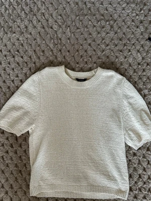 Beige stickad tröja från Lindex - Säljer en beige stickad tröja från Lindex i storlek XS. Tröjan har korta ärmar, rund hals och ribbade detaljer vid hals, ärmslut och nederkant. Perfekt för dig som gillar enkel och stilren design med mjukt material.