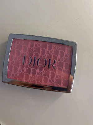 Dior Rosy Glow Rouge 001 Pink - Dior Rosy Glow Rouge i färgen 001 Pink. Ett pressat puderrouge med intensivt rosa nyans som ger en fräsch och naturlig glow. Kommer i en lyxig rektangulär dosa med silverdetaljer och Dior-logga. Perfekt för att ge kinderna en pop av färg.