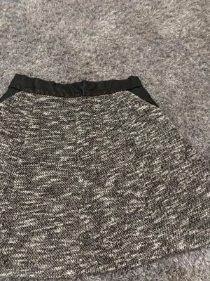 Svartvit kortkjol från Newyorker - Säljer en svartvit kortkjol från Mee Yorker i storlek 40/L. Kjolen har ett melerat mönster, bred midja i fejkskinn och dragkedja bak. Materialet känns tjockare och lite stickat, vilket ger en snygg struktur. 💕
