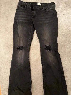 Svarta jeans med hål från Nelly - Svarta jeans från Nelly med slitna hål på båda knäna och klassisk femficksdesign. Jeansen har en rak passform och är tillverkade i jeansmaterial. Snygga detaljer på bakfickorna med broderad våg. Perfekta för dig som gillar en edgy stil. Jeansen är använda 1 gång och har mycket bra skick. Köpta för 699 och tänker mig 400 för dem