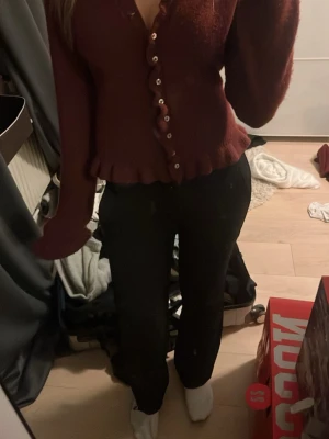 Vinröd kofta med volang och knappar - Säljer en vinröd kofta med dekorativa volanger  och en knapprad. Koftan har långa ärmar och är  med en söt volangkant nedtill. Säljer för att den inte kommer till användning