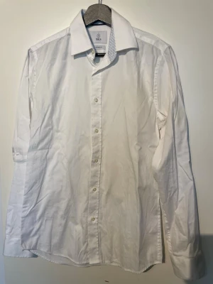 Vit skjorta från Bläck - Klassisk vit skjorta med lång ärm och knappar framtill. Skjortan har en stilren design med vanlig krage och är tillverkad i bomull för en skön känsla. Perfekt till jeans eller chinos för en clean look.