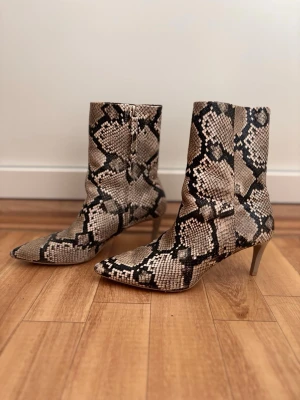 Boots - Snygga boots med ormmönster i beige, svart och bruna toner. Skorna har spetsig tå och smal klack. Perfekta för dig som vill sticka ut med din stil.