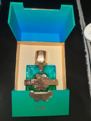 Aromatix parfym från French Avenue - Lyxig parfymflaska från French Avenue i turkost glas med guldfärgade detaljer och lock. Flaskan har en unik, geometrisk form och levereras i en elegant turkos och guldig presentförpackning. Märket Aromatix syns tydligt på framsidan. Helt ny bara provtestad