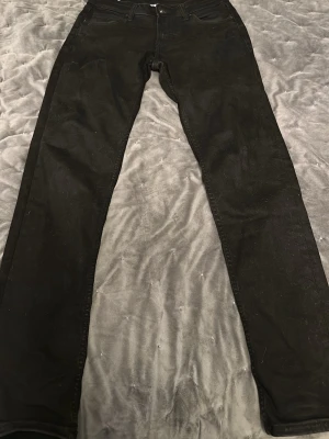 Svarta raka jeans från Levi's - Säljer ett par svarta jeans från vailent med klassisk rak passform och femficksdesign. Jeansen har normal midja och är tillverkade i slitstarkt bomullsmaterial. Perfekta till en avslappnad stil och funkar året runt. Priset är inte hugget i sten så om det är någon fundering om priset eller byxan är det bara att ta kontakt 