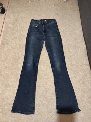 Levi's 725 High Rise Bootcut Jeans - Snygga blå Levi's 725 high rise bootcut jeans med klassisk femficksdesign och hög midja. Jeansen har en bootcut passform som ger en schysst siluett och är tillverkade i mjukt denimtyg. Perfekta för dig som gillar en tidlös och trendig look.