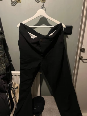 Svarta kostymbyxor med rak passform från Zara - Stilrena svarta kostymbyxor från Zara med klassisk rak passform. Byxorna har knapp- och dragkedjestängning samt vita detaljer på insidan av linningen. Perfekta för en dressad look.