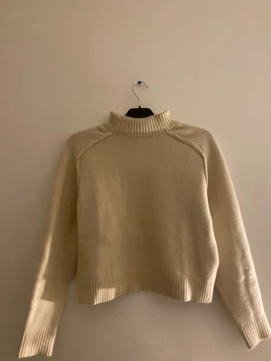 Beige stickad tröja från H&M - Säljer en beige stickad tröja från H&M med hög krage och ribbade muddar vid hals, ärmslut och nederkant. Tröjan har en avslappnad passform och är perfekt för kyliga dagar. Enkel och stilren design som passar till det mesta. Andävd 1gång!!!