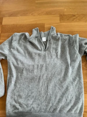 Grå halvzip tröja från Lindex - Snygg grå tröja från Lindex med halvzip och hög krage. Tillverkad i mjukt material och har ribbade muddar vid ärmslut och nederkant. Perfekt för en avslappnad och stilren look. Passar sig som är 146/152cm